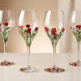 Load image into Gallery viewer, Four clear wine glasses with stems and round bases decorated with painted red flowers, green leaves, and small blue and yellow accents, arranged on a light surface against a soft beige background.
