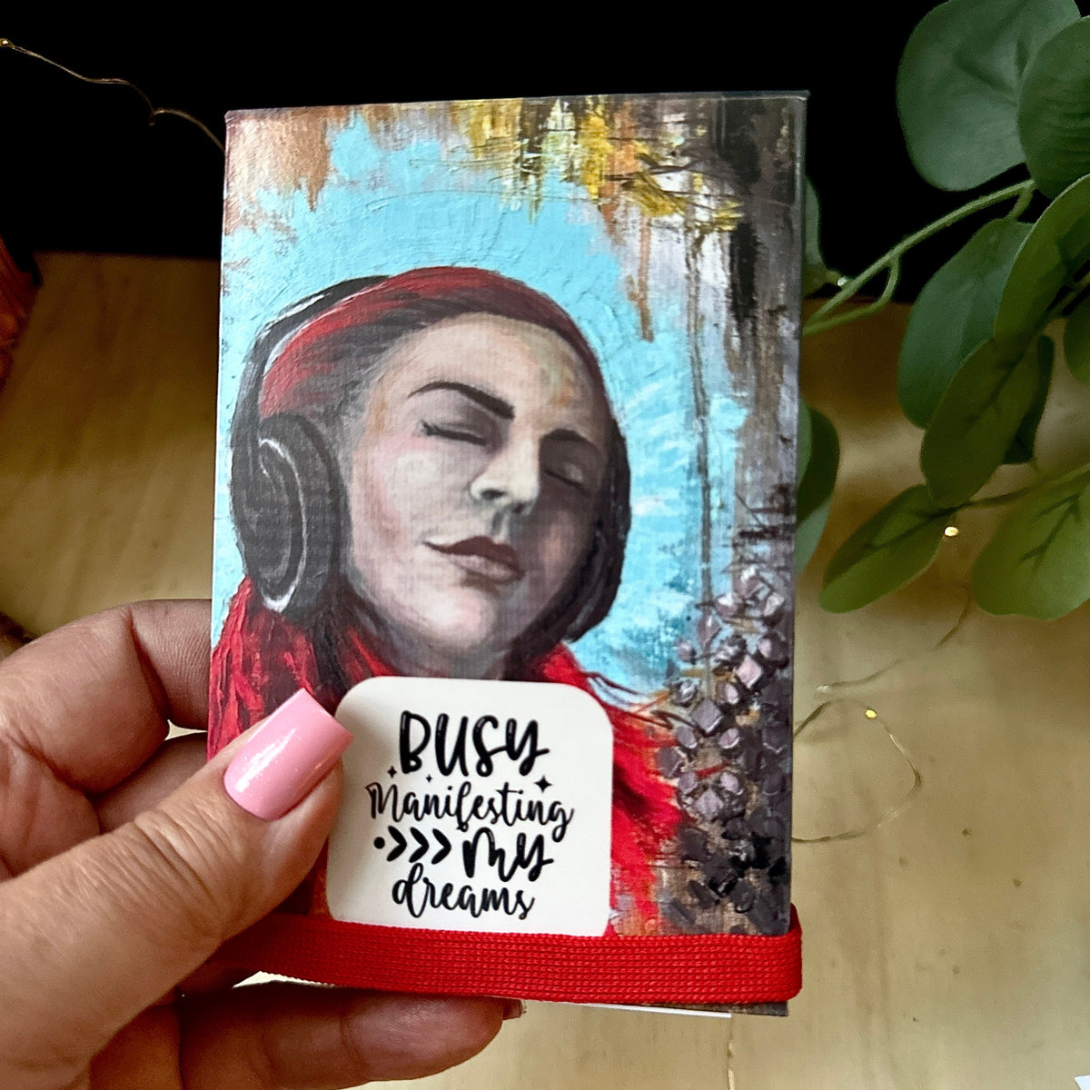 Notepad holder with Lost in Sound original artwork print with inspiration message and the text on the white space.'BUSY Manifesting >>> my dreams.' 