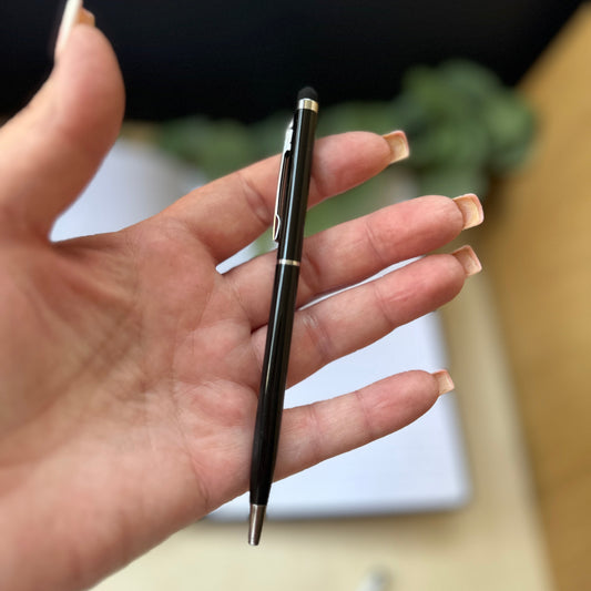 A black ballpoint pen with silver accents held in a person's hand, with a blurred indoor background.