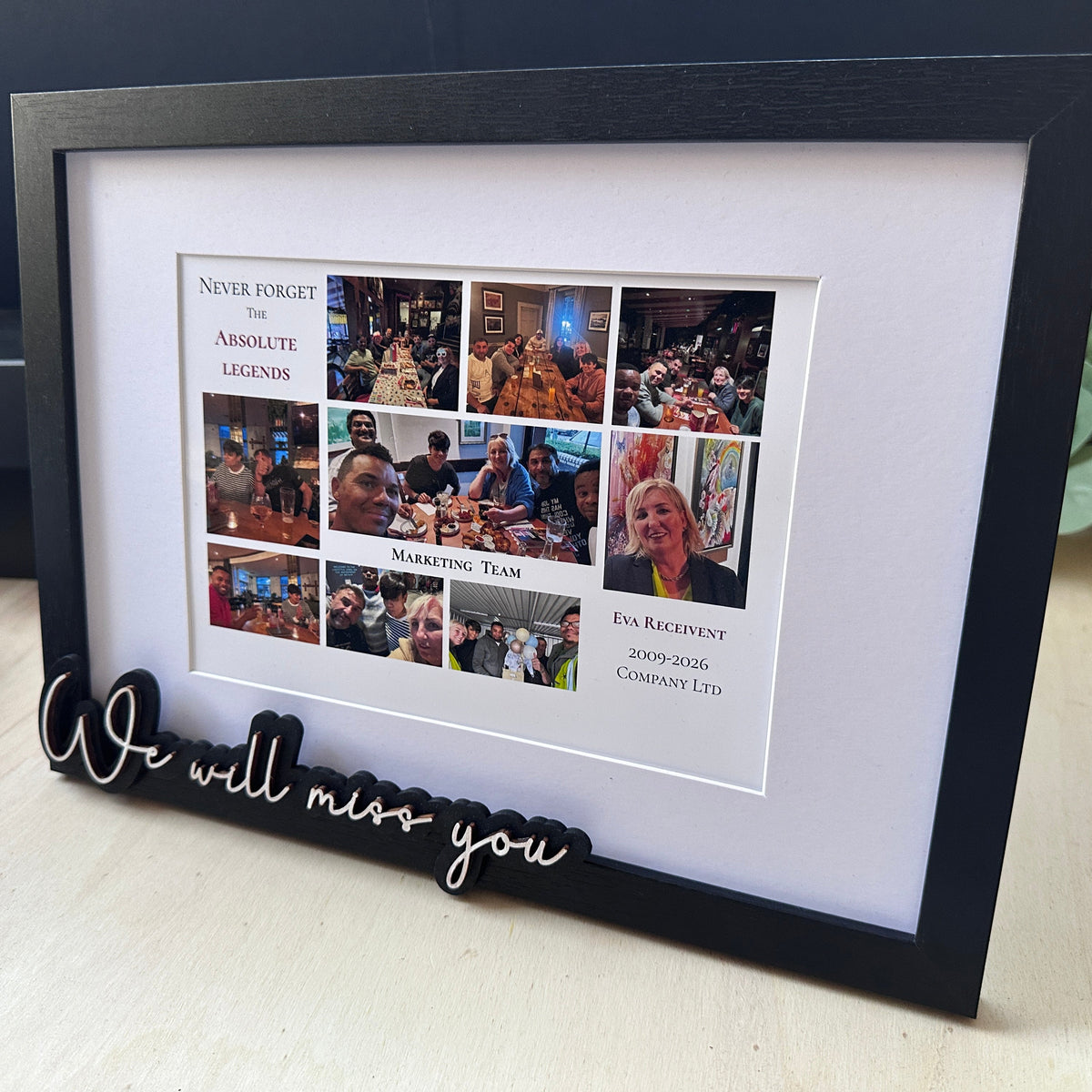 A black rectangular Farewell photo frame with a white mat, containing a collage of company/team photos and printed text, displayed on a light wood surface. A black 3D cutout at the bottom reads 'We will miss you'.