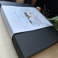 Load image into Gallery viewer, A black textured rectangular box with a white printed ibelly band around the gift box, photographed at an angle on a light beige surface.
