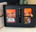 Load image into Gallery viewer, A black gift set box containing a black fountain pen with silver trim and notepad holder with matching floral bookmarks with tassels, displayed on a light wood surface.
