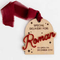 Load image into Gallery viewer, A personalized wooden arch-shaped gift tag with 3d name hanging with a burgundy ribbon loop, featuring engraved text that reads 'SPECIAL DELIVERY FOR: Roman TO OPEN ON DECEMBER 25TH' with decorative star details.
