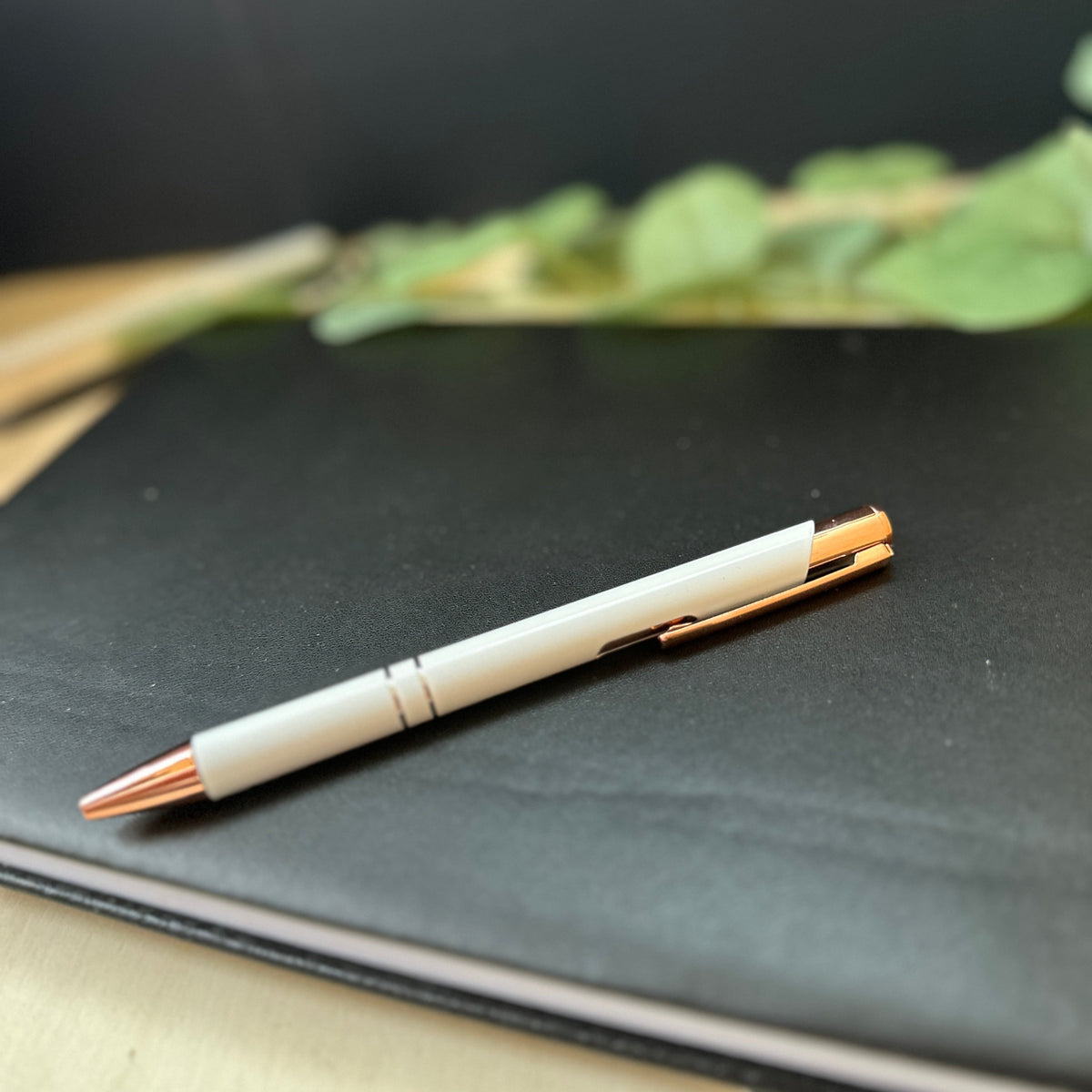 A slimball pen with a white barrel and rose gold accents, resting diagonally on a black notebook.