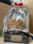 Load image into Gallery viewer, A personalized birthday gift basket wrapped in clear cellophane, featuring a black decorative base, a round wooden coaster, a small glass with floral details, and a pink ribbon with a gold 'Hello 50th' topper. The front label is personalized with the name  and 'Happy 50th Birthday'.
