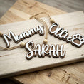 Load image into Gallery viewer, Personalized wooden hanging ornaments spelling 'Mommy Sarah' and 'Ollie Sarah' with a paw print, shown on a light wood board over a rustic wooden surface.
