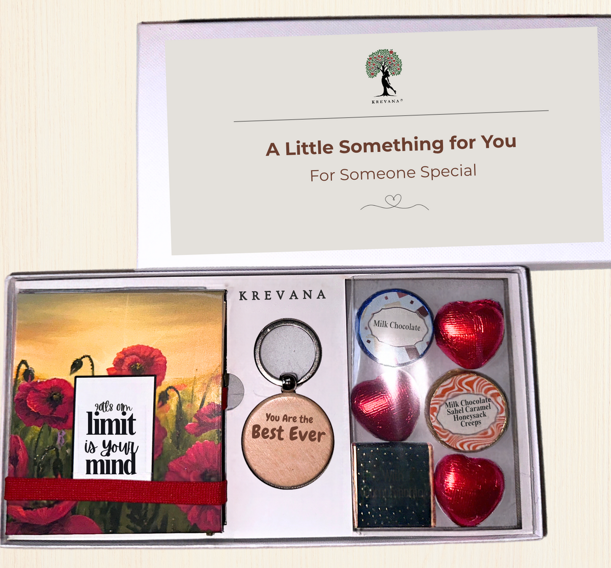 A Krevana gift box set displayed open on a light beige background. The set includes a red poppy sticky notepad with the quote 'It's your own limit is your mind', a round wooden keychain reading 'You are the Best Ever', milk and dark chocolate hearts, a small tin of gourmet chocolates, 