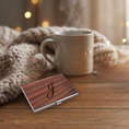 Load image into Gallery viewer, A rectangular wooden card case with a silver metal clasp and an engraved cursive monogram, resting on a wooden table next to a steaming mug and a knitted blanket.
